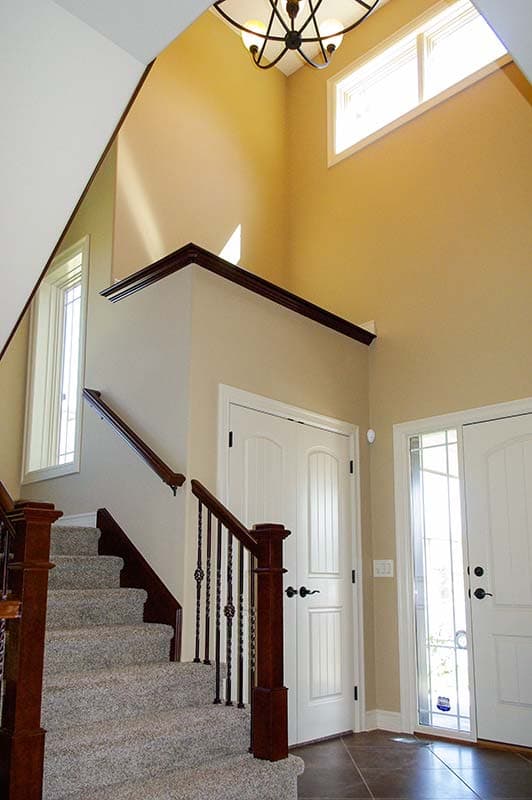 Two-story foyer with carpeted staircase, wooden banister, transom windows, and paneled doors.