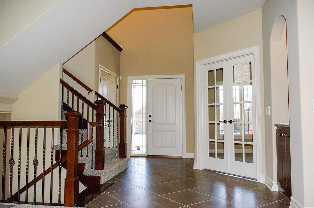 Interior foyer with vaulted ceiling, staircase with wood railing and metal spindles, front door with sidelight, and double French doors.