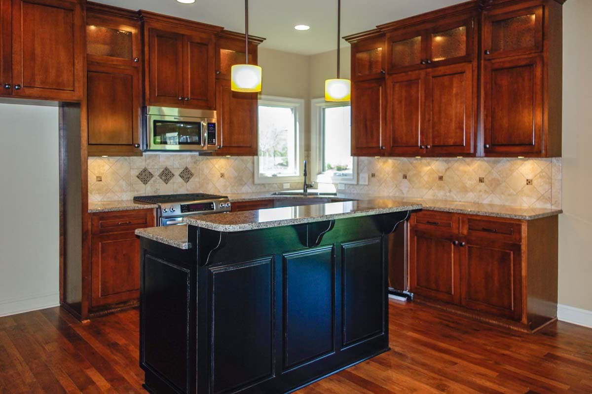 Kitchen with wood cabinets, granite countertops, island with dark cabinetry, stainless steel appliances, and tile backsplash.