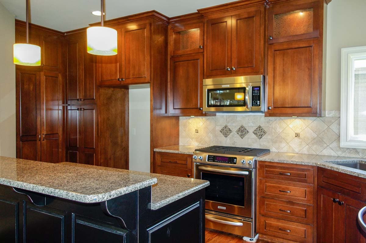 Kitchen interior with cherry wood cabinets, granite countertops, stainless steel range, microwave, and island with dark wood base.