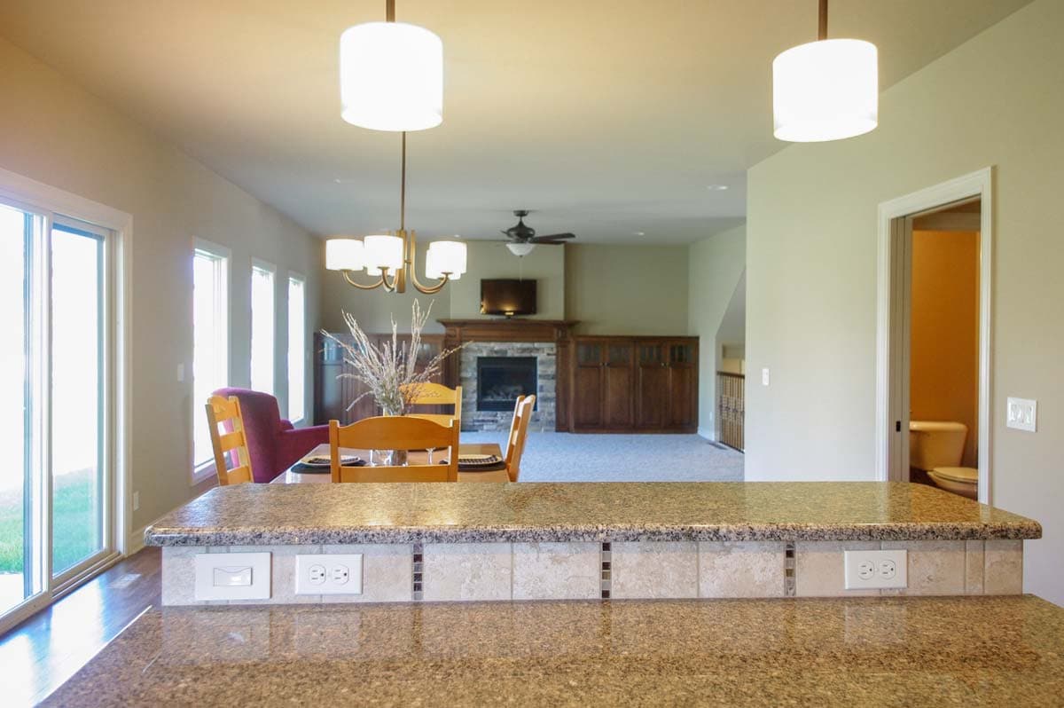 Interior view of a house showing a kitchen counter, dining area, great room with fireplace, and a bathroom.