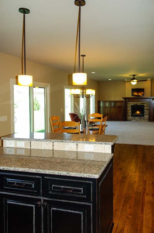 Kitchen island with granite countertop adjacent to dining area and open living space with fireplace.