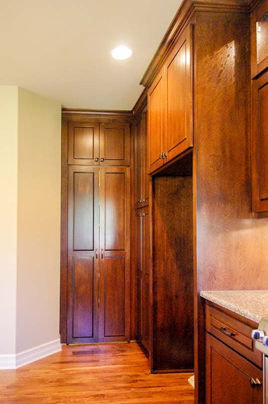 Corner view of a kitchen with dark wood cabinetry, including tall pantry cabinets and an open appliance niche.