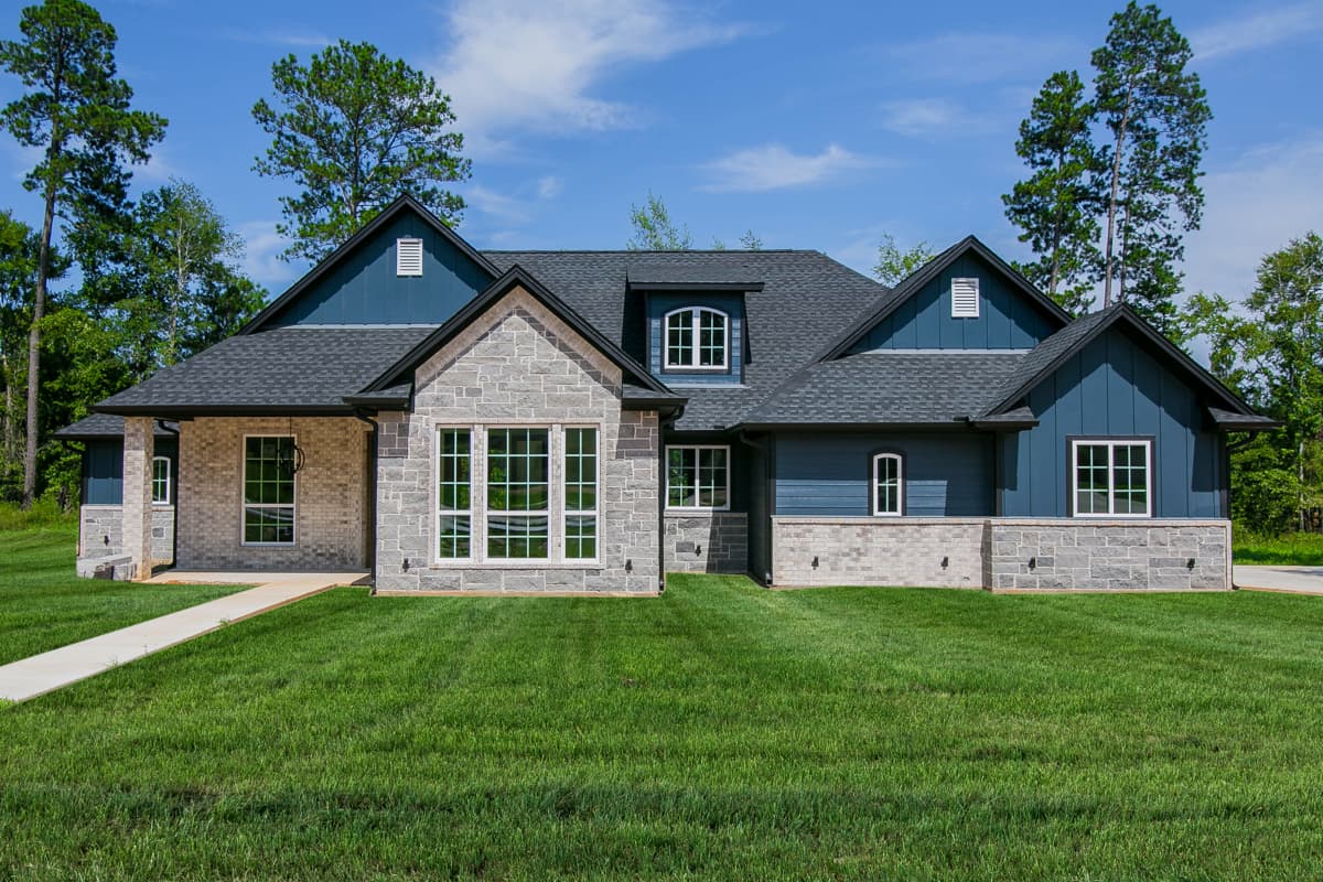 House plan exterior. Two-story home with a gabled roof, stone facade, dormers, and an attached garage.