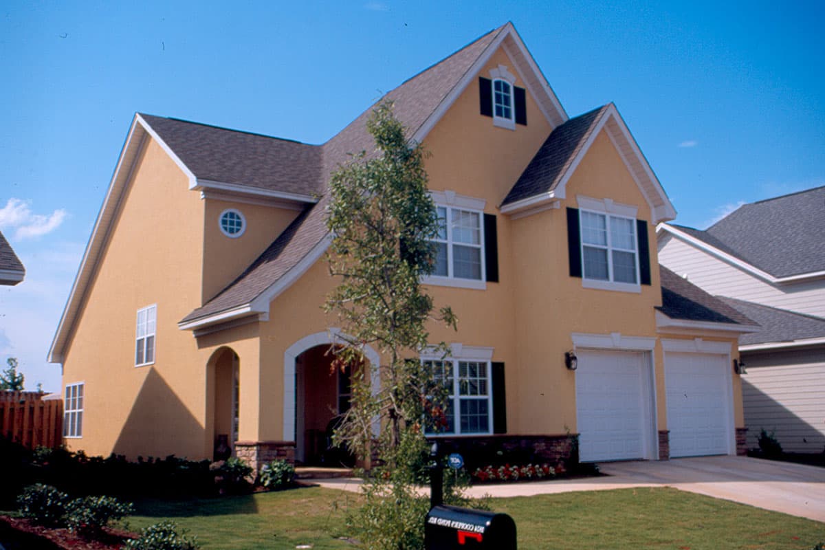 House plan exterior: Two-story home with arched entry, dormer, and a double garage. Features stucco siding and multiple gables.