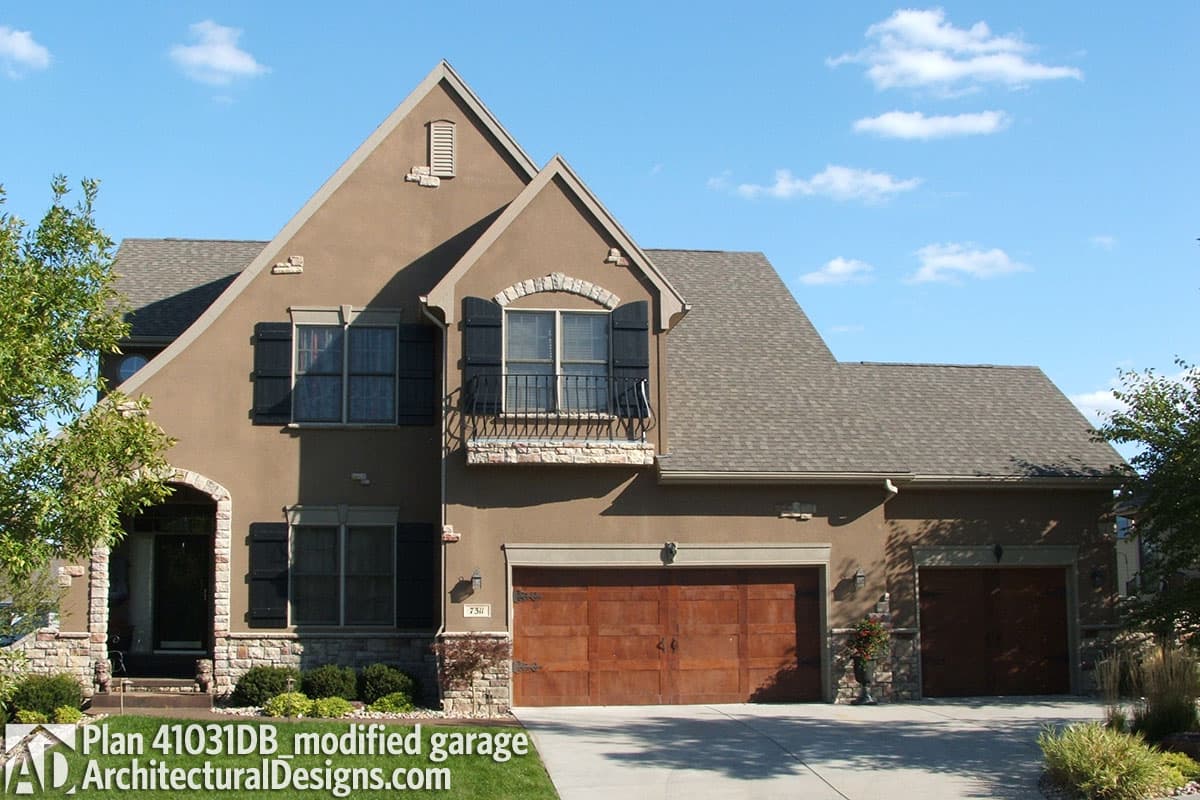 House plan exterior: Two-story home with stucco exterior, arched entryway, prominent gables, dormer window, and a three-car garage.
