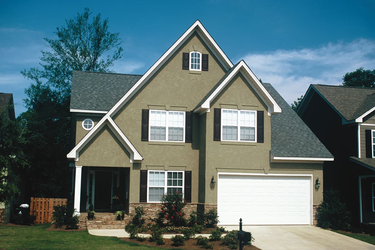 House plan exterior: Two-story stucco home with gabled dormer, covered porch, and attached garage.