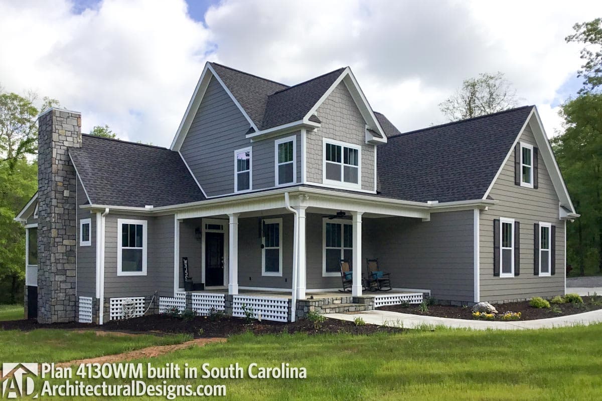 House plan exterior of a two-story home with a wraparound porch, stone chimney, and multiple gables.