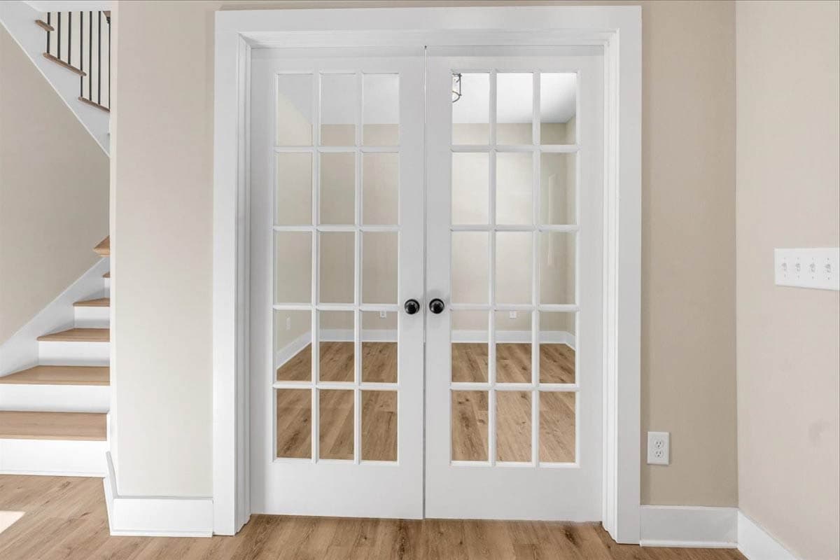 Interior view of white double doors with multiple glass panes, opening to a room with wood floors. Staircase visible to left.