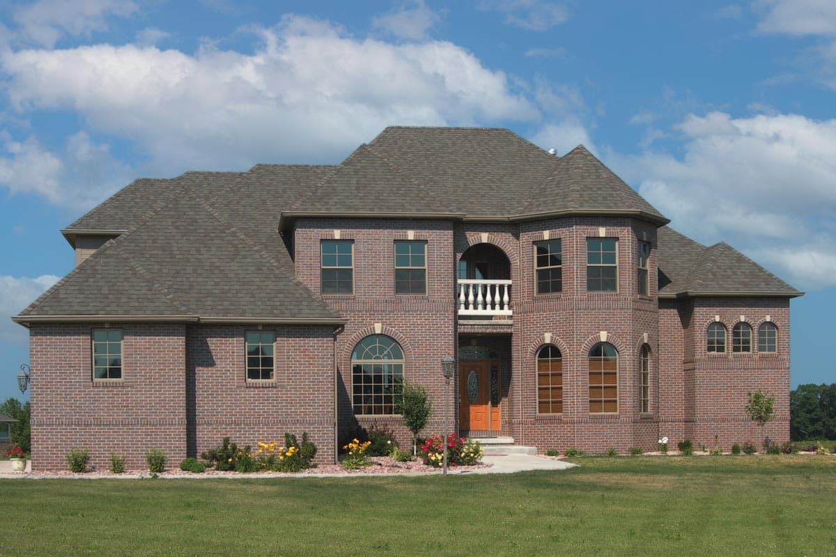 Two-story brick house plan with multiple gables, arched windows, and a prominent second-story balcony with railing.