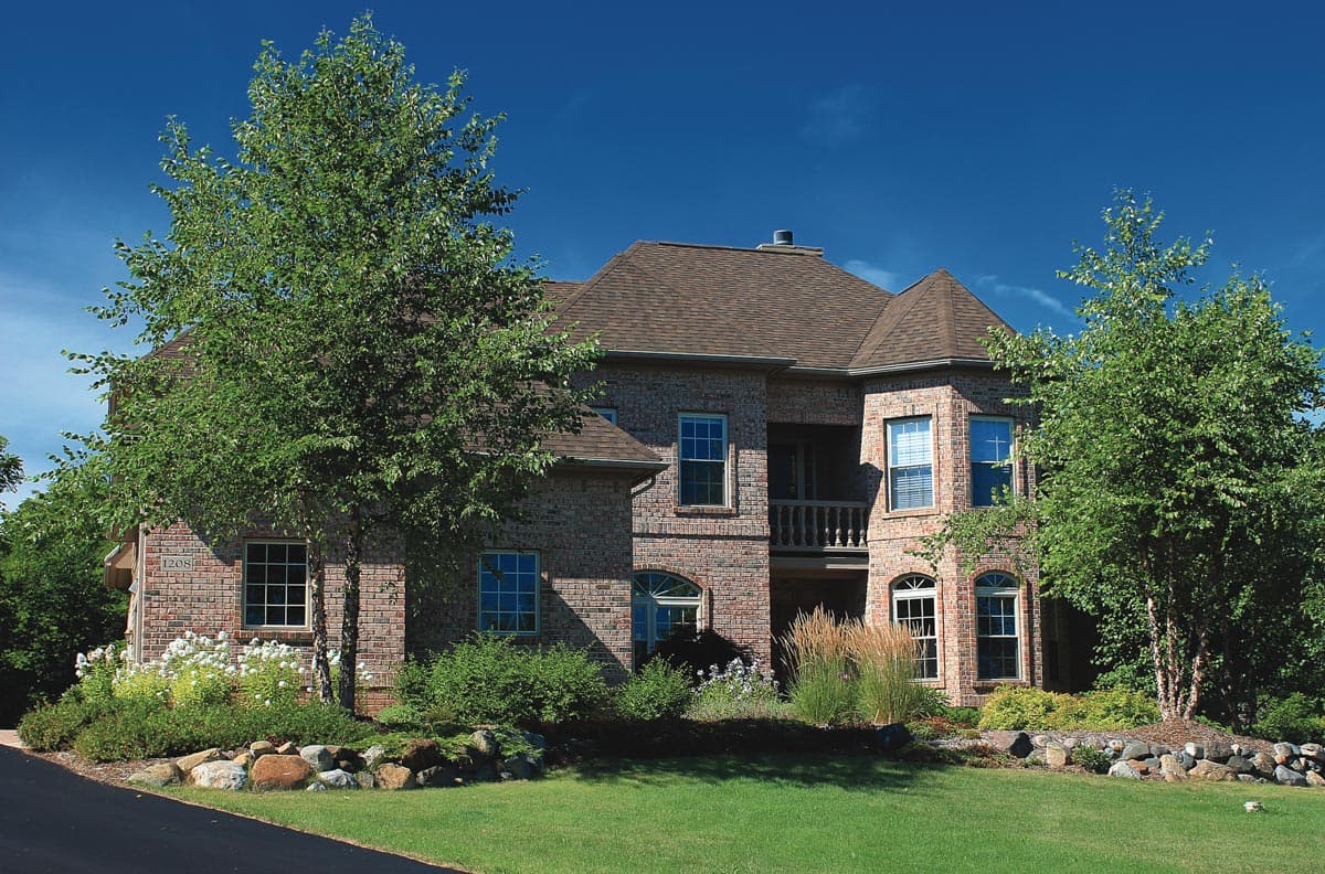 House plan exterior: two-story brick home with varied rooflines, upper balcony, and arched window details.