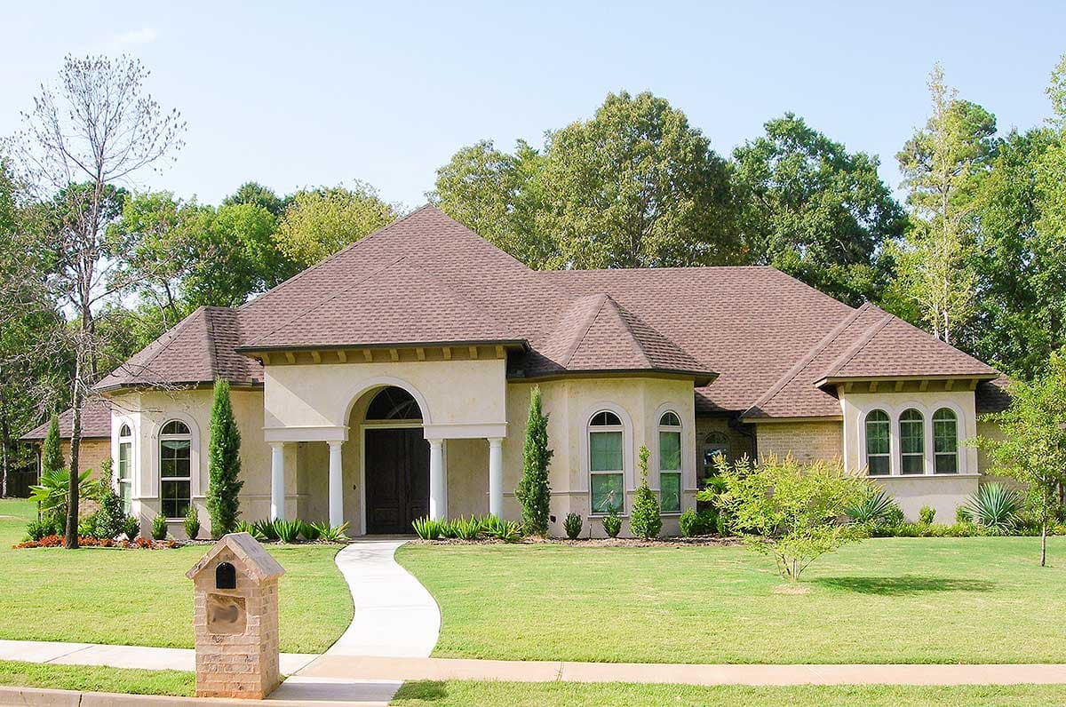 House plan exterior. Two-story, stucco facade with a gable roof, arched entryway, and multiple arched windows. Stone mailbox in front.