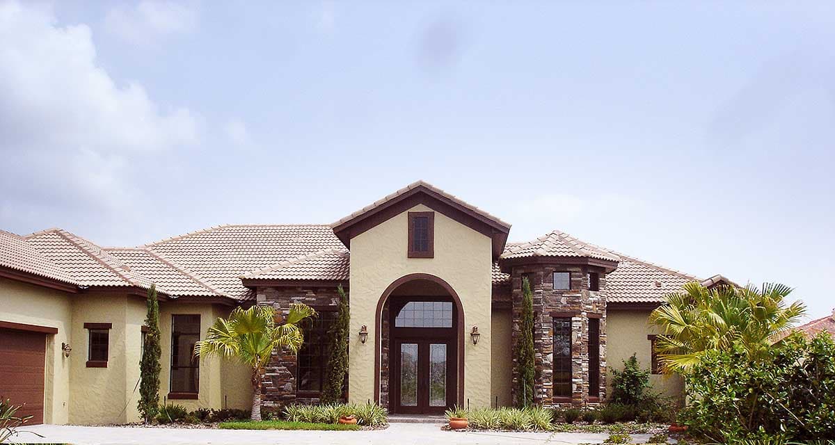 House plan exterior: Mediterranean style, one story, stucco finish, stone accents, arched entryway with double doors, tiled roof.