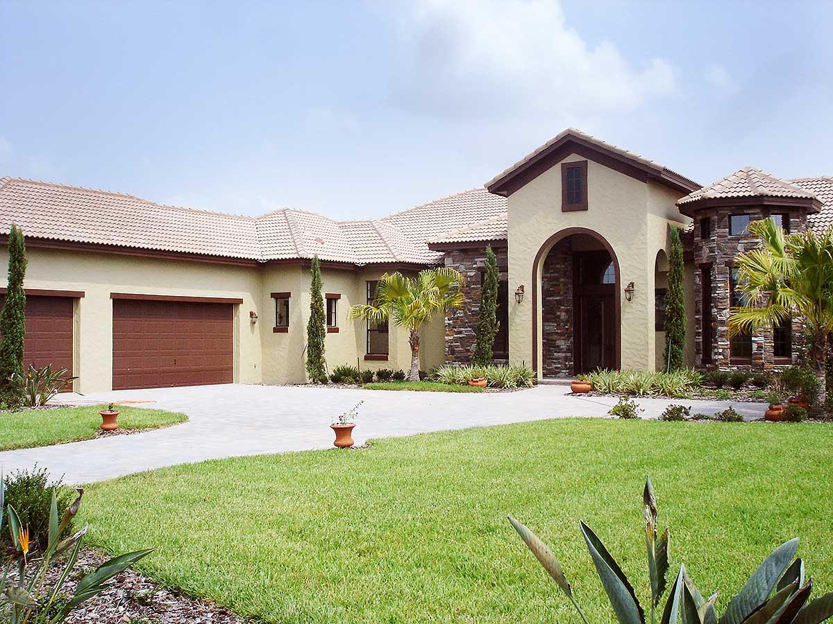 House plan exterior: Ranch style with three-car garage, arched entryway with stone accents, and tile roof.
