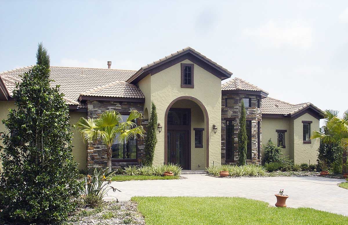House plan exterior: Single-story home with arched entryway, stone accents, tiled roof, and varied gables.