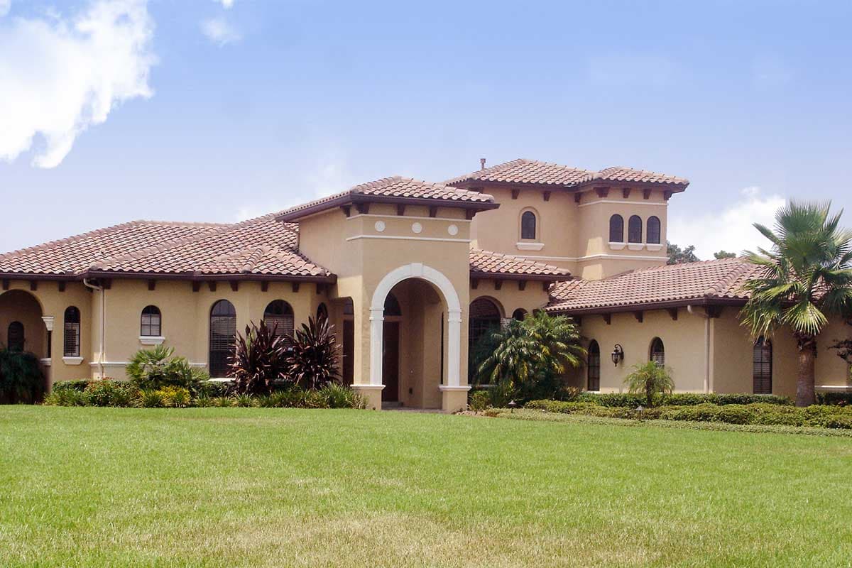 House plan exterior in Mediterranean style with arched entryway, clay tile roof, and multiple gables.