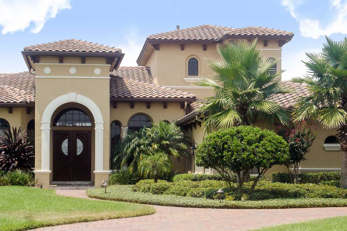 Mediterranean style house plan exterior with arched entry, double doors, tile roof, and lush landscaping.