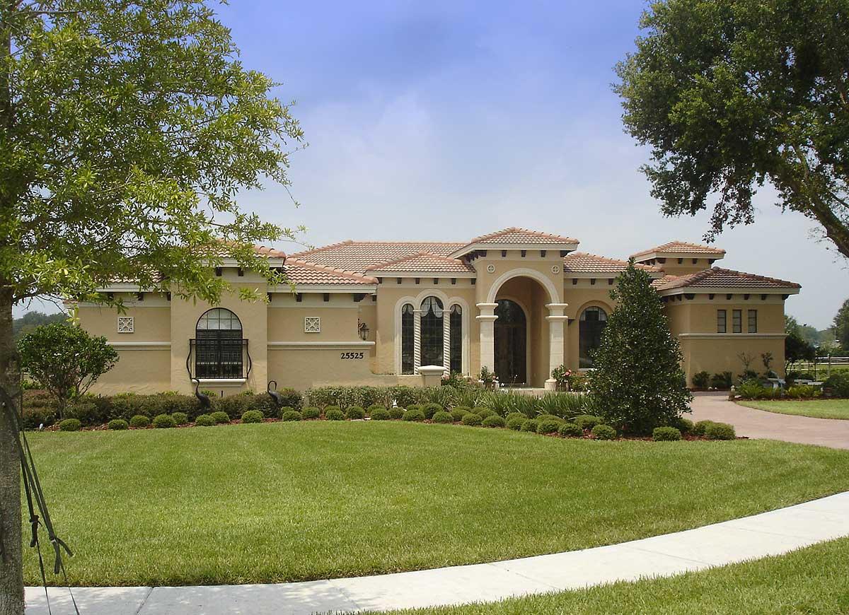 House plan exterior in Mediterranean style with arched entryway, arched windows, and tile roof.