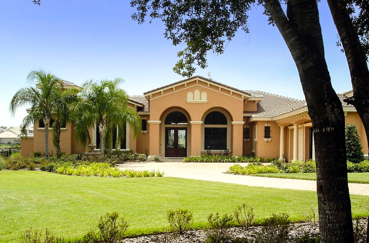 House plan exterior. Two-story Mediterranean-style home with arched entry, columns, and tile roof. Features a circular drive and manicured lawn.