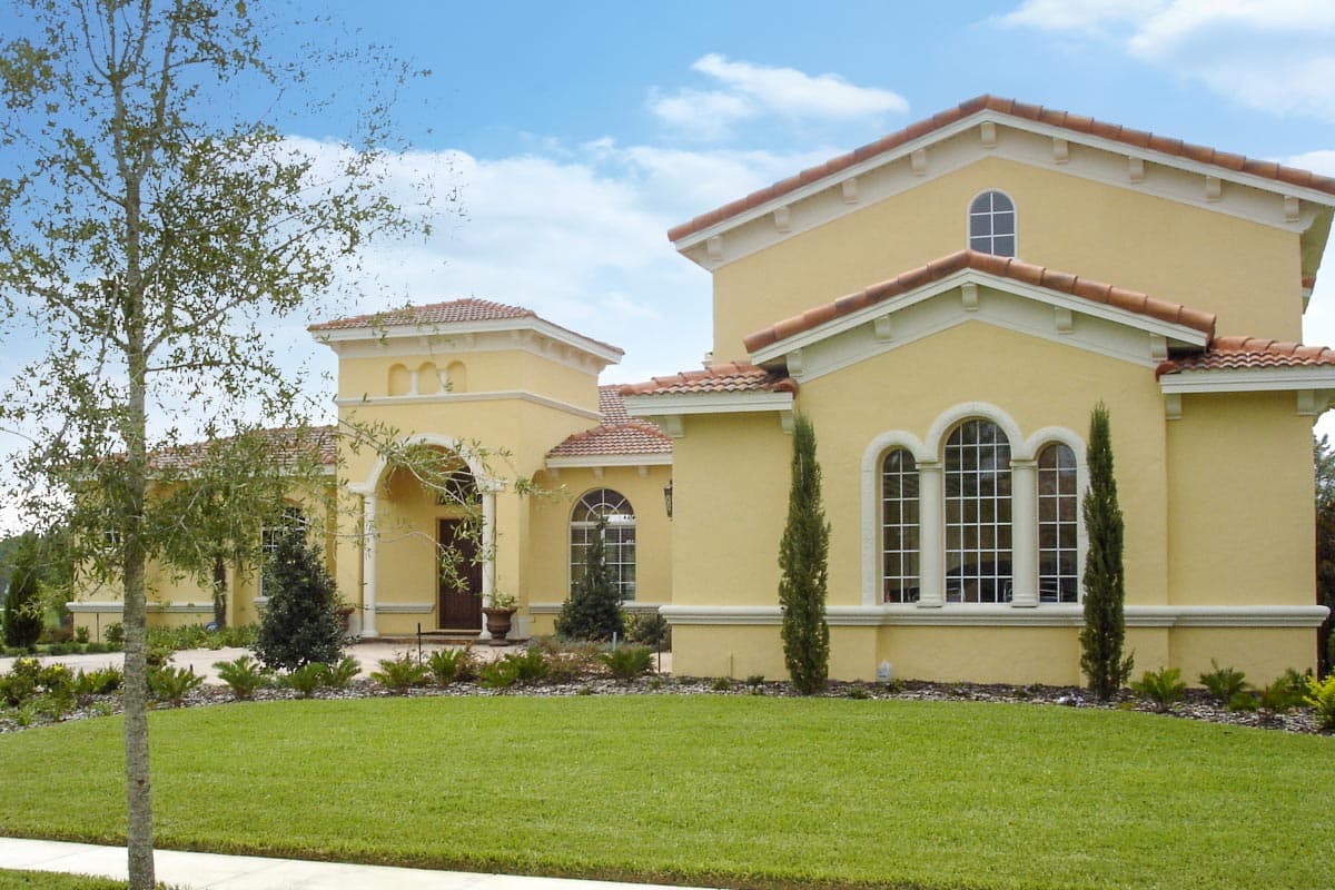 House plan exterior: Yellow stucco, two stories, arched windows, tile roof, and covered entryway.