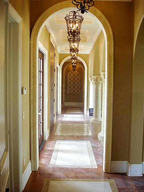 Interior hallway with arched doorways, decorative light fixtures, patterned floor inlays, and classical columns.