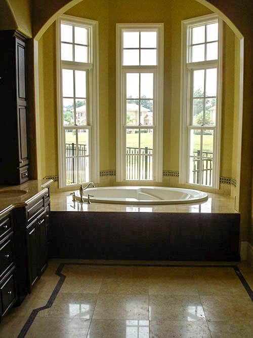 Bathroom with oval soaking tub, dark wood cabinetry, marble flooring, and arched window bank.