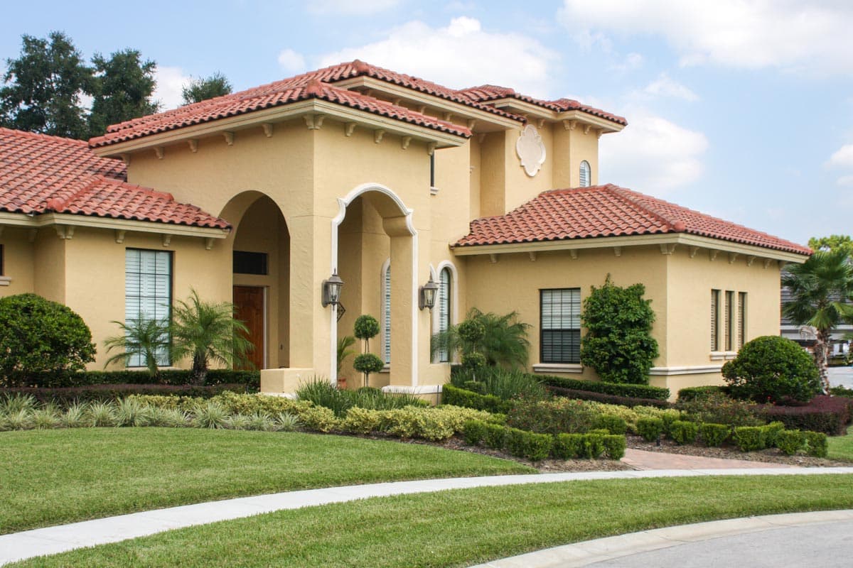 House plan exterior: Mediterranean style, stucco finish, red tile roof, arched entryway, multiple gables, and large windows.