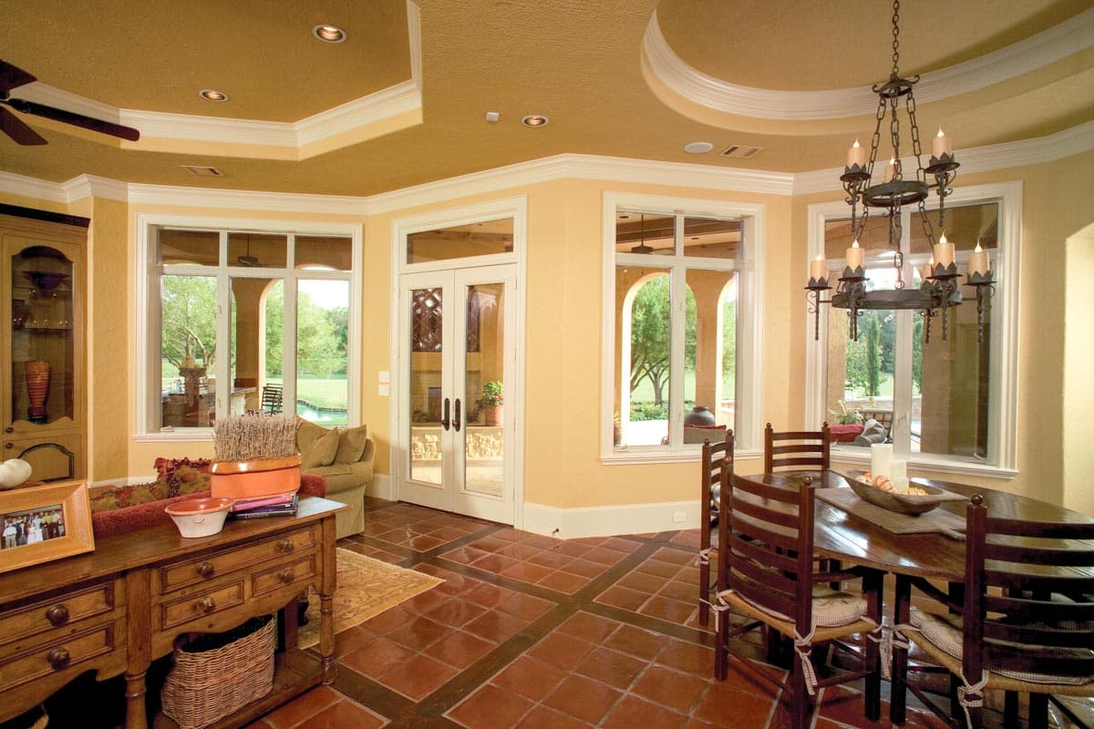 Dining area with table, chairs, chandelier, french doors, and large windows overlooking a yard and pool.