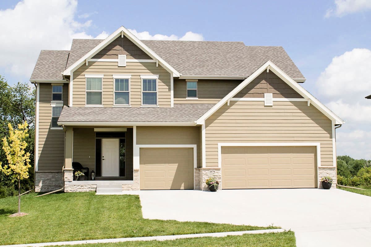 Two-story house plan exterior with a covered front porch, gable dormers, siding, and a three-car garage.