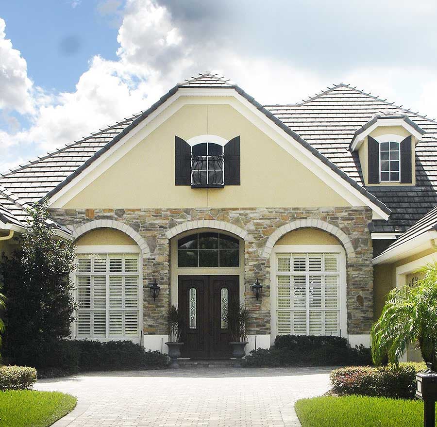 House plan exterior: Two-story home with stone facade, arched entry, double doors, gable dormer, and tile roof.