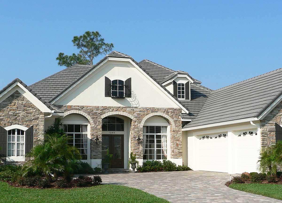 House plan exterior: Two-story home with stone accents, arched entryway, dormer windows, and a side-facing two-car garage.