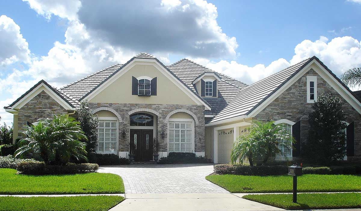 House plan exterior: one-story home with stone accents, gabled rooflines, arched entryway, dormer, and attached garage.