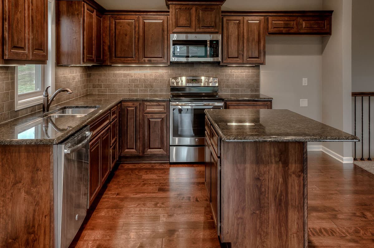 Kitchen with dark wood cabinets, granite countertops, stainless steel appliances, subway tile backsplash, and island.