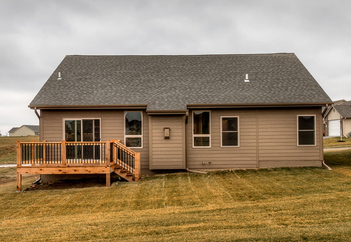 House plan exterior: single-story tan home with a wooden deck, steps, and multiple windows.