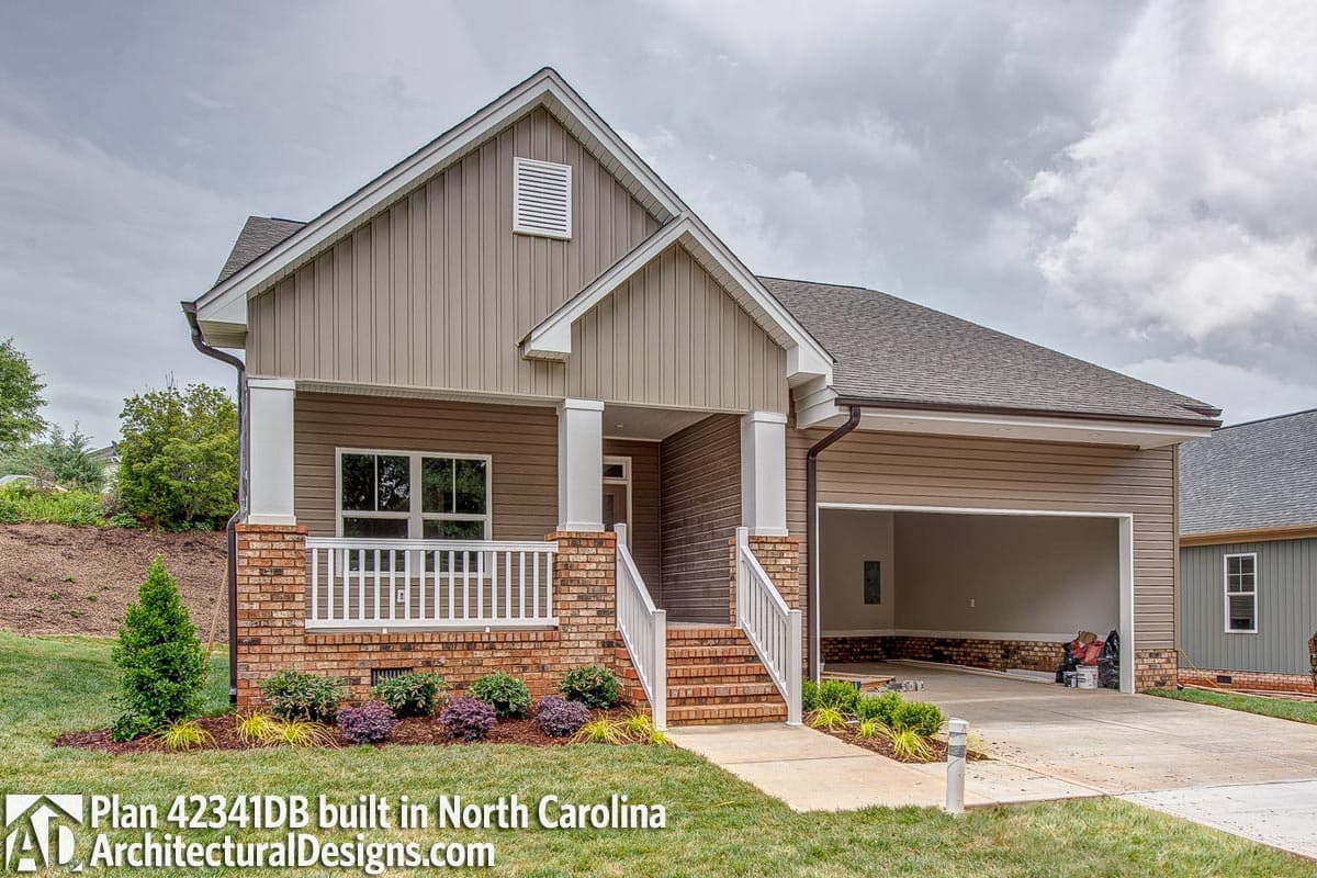 House plan exterior with brick accents, covered porch with white railing, vertical siding, and attached two-car garage.