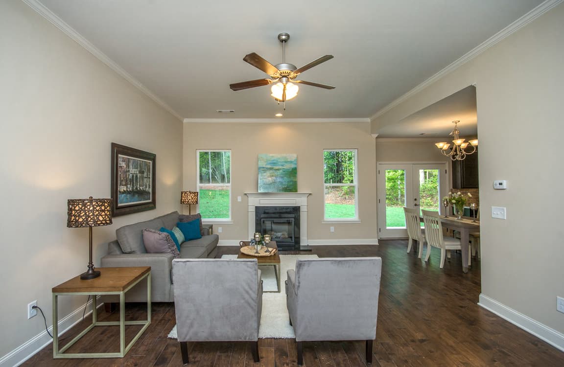 Interior view of living room with fireplace, two windows, sofa, chairs, and adjacent dining area with doors.
