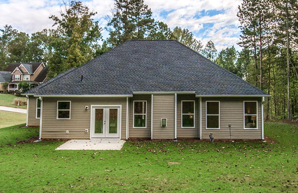 House plan exterior: Two-story house with dark asphalt roof, vinyl siding, and double glass doors leading to a concrete patio.