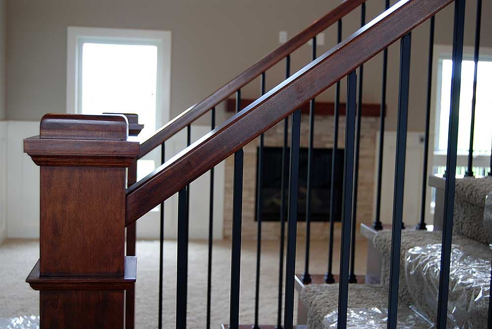 Interior view of staircase with dark wood handrail, square newel post, and black metal balusters.