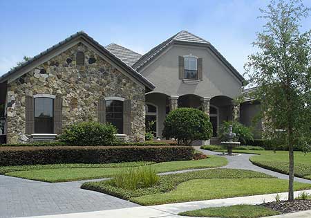 House plan exterior showing a stucco and stone facade with arched windows, a covered entryway with columns, and a pitched tile roof.