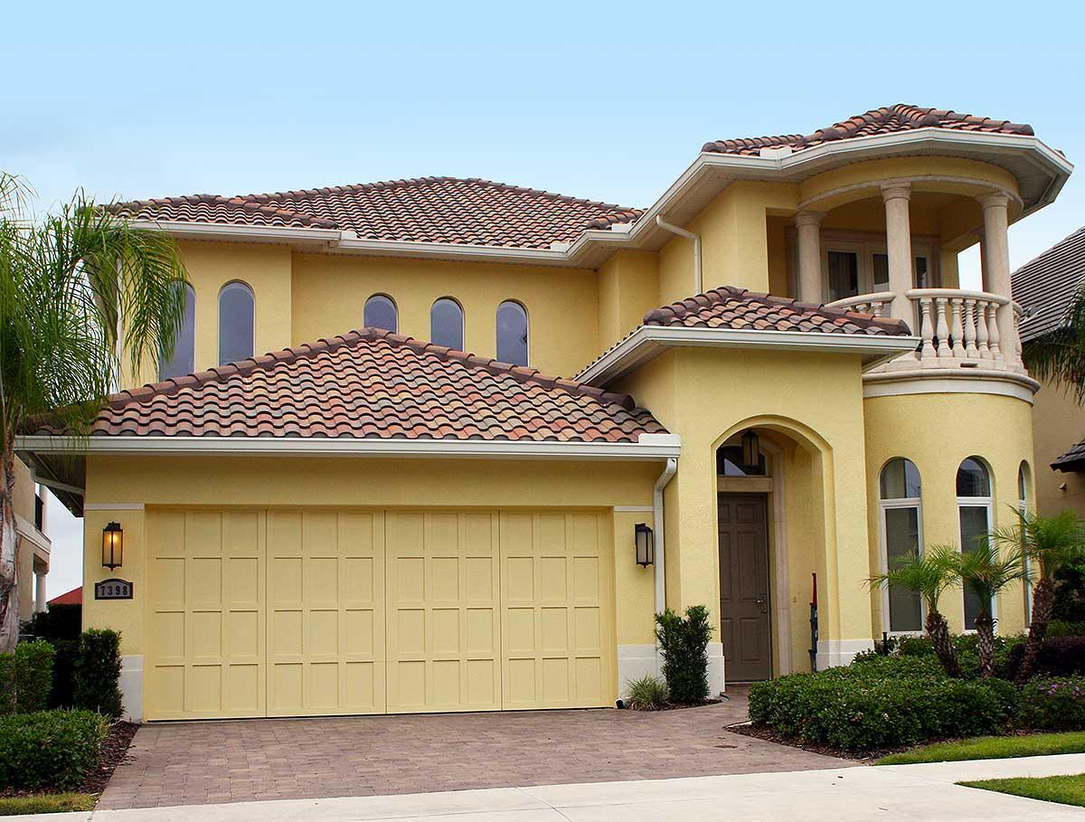 House plan exterior: Two-story home with stucco finish, arched entryway, multiple gables, and a second-story balcony with columns.
