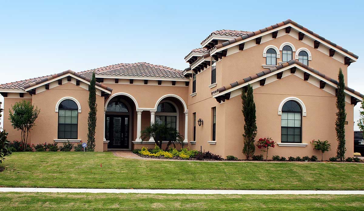 House plan exterior: Single-story home with tile roof, arched entryway, multiple arched windows, and decorative gable eaves.