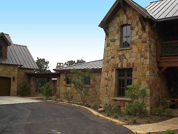 House plan exterior with stacked stone facade, metal roof, gables, dormers, and an attached garage. Two stories visible on main tower.