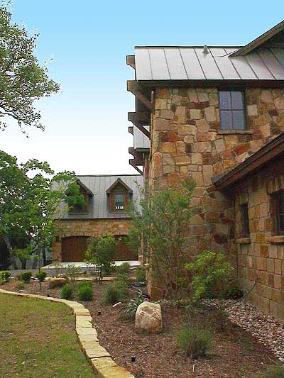 House plan exterior showing stone facade, metal roof, dormers, and a multi-car garage with wood doors.