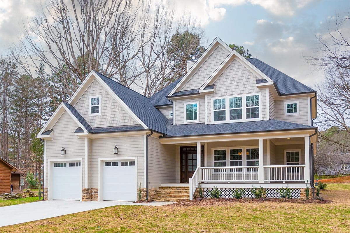 House plan exterior. Two-story, Craftsman-style home with a front porch, gables, and a two-car garage. Features shingle siding and a dark roof.