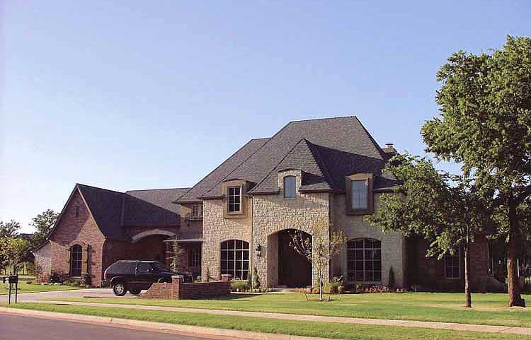 House plan exterior: two-story residence with stone and brick facade, arched entryway, multiple gables, and dormer windows.