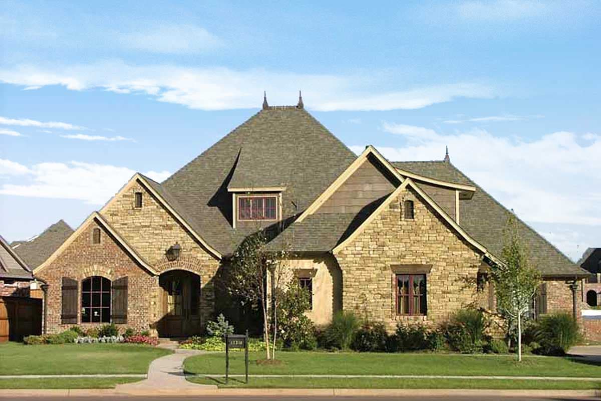 House plan exterior: one-story home with stone and brick facade, arched entryway, multiple gables, and dormer window.