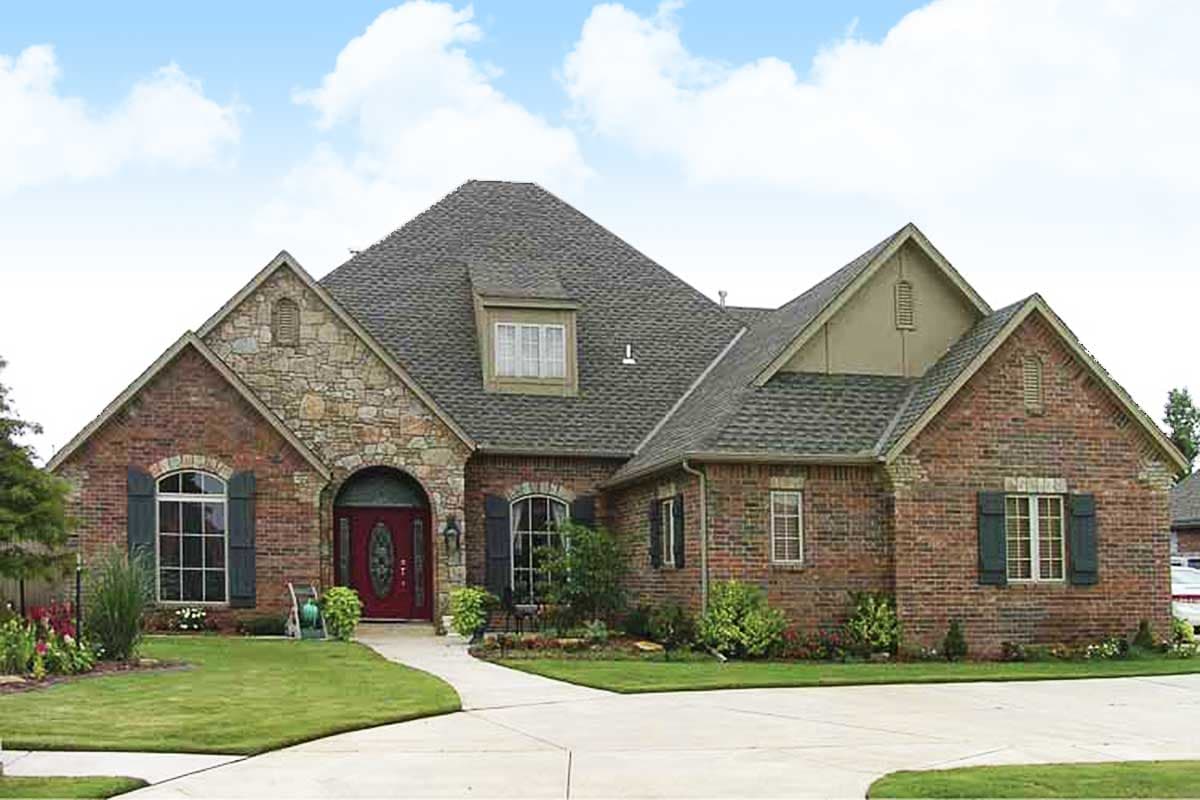 House plan exterior: brick and stone facade, arched entry, gable dormer, multiple gables, and pitched roof.