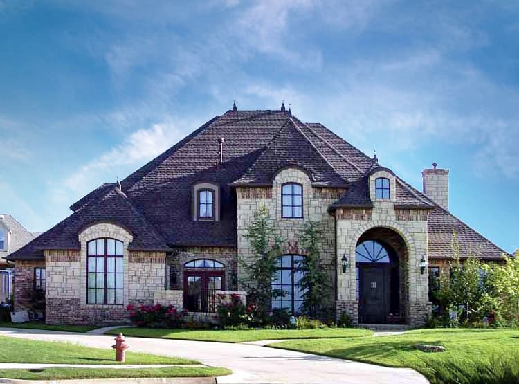House plan exterior featuring stone and brick facade, arched entryway with double doors, multiple gables, and dormer windows.