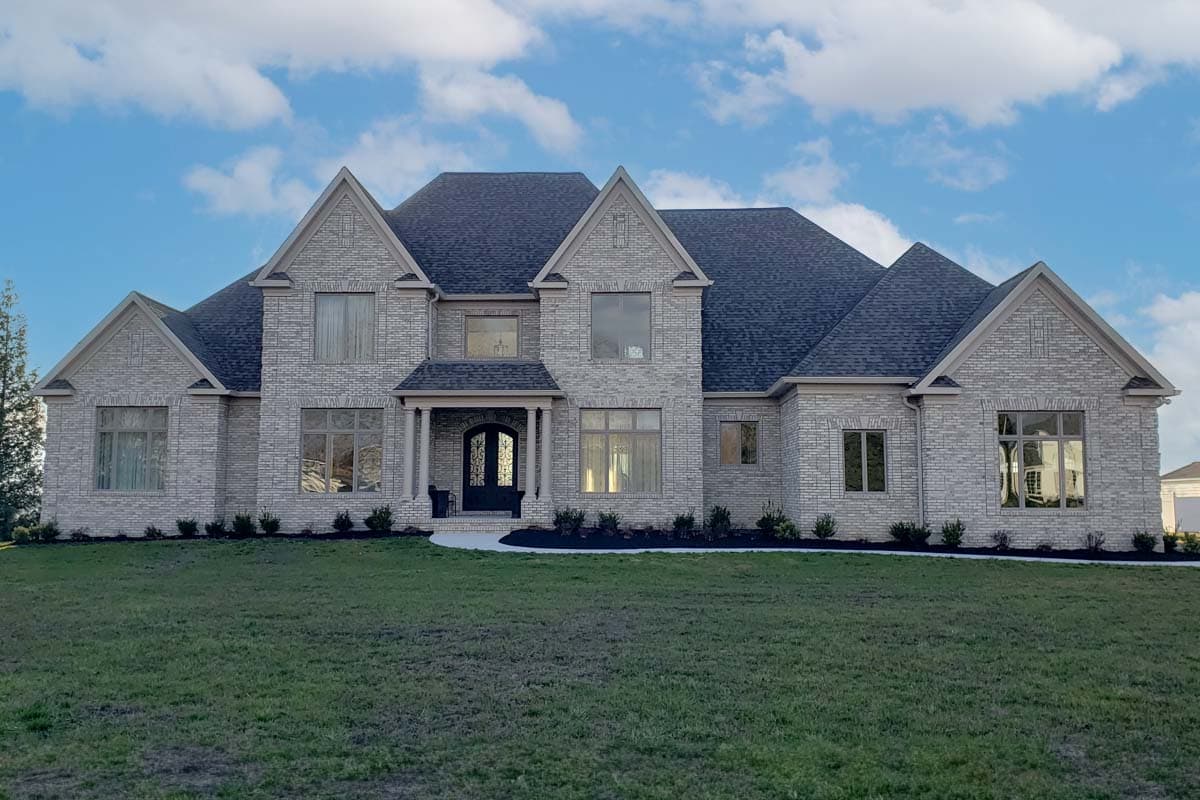 House plan exterior with two stories, multiple gables, and a front porch. Features include brick facade and large windows.