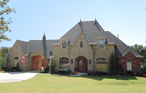 House plan exterior: two-story French Country style home with stone and brick facade, arched entryway, multiple gables, and dormer windows.